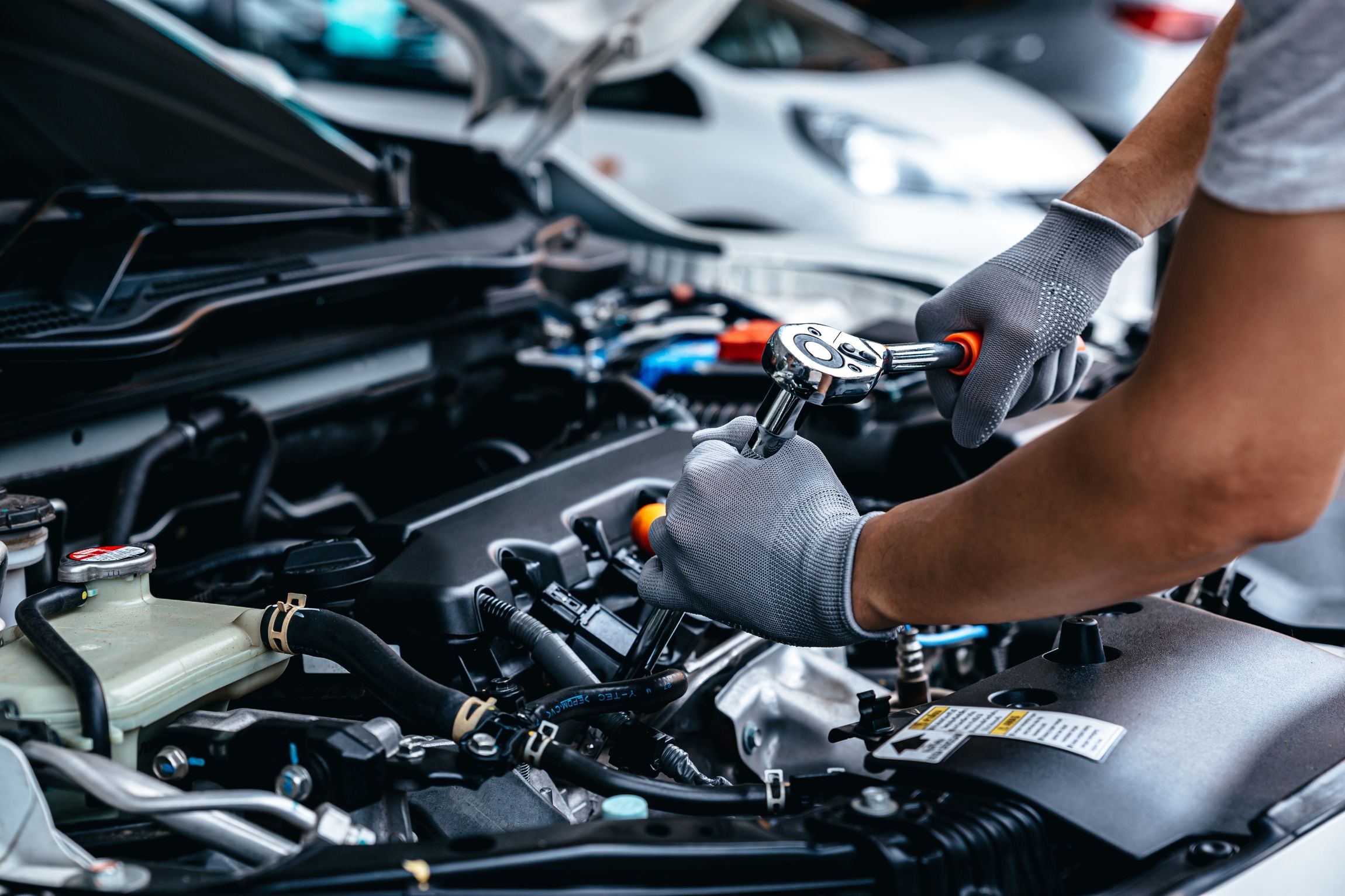 Person mit grauen Handschuhen arbeitet mit Ratsche an einem Motorraum eines Autos
